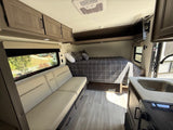 Modern RV rental interior with a cozy bed, sofa, kitchenette, and overhead cabinets. Ideal for road trips.