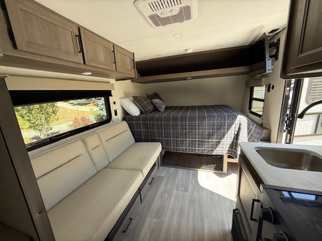 Modern RV rental interior with a cozy bed, sofa, kitchenette, and overhead cabinets. Ideal for road trips.