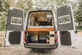 Open rear doors reveal a custom camper van conversion, ideal for rv rental adventures. Features a raised bed, ample storage.