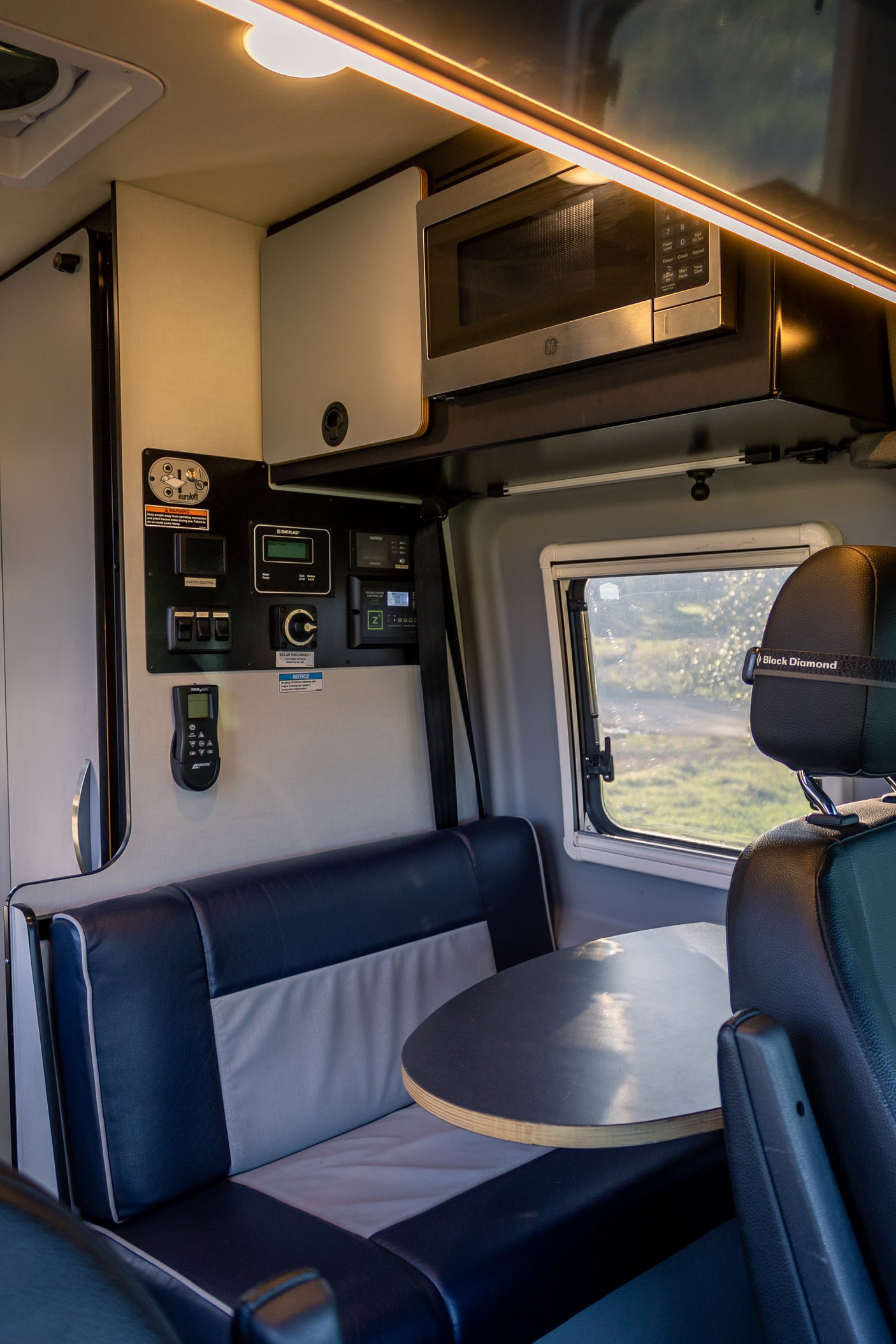 RV rental interior: Dinette, overhead microwave, and wall-mounted tech controls in a modern camper van.
