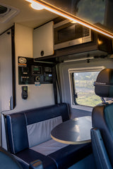 RV rental interior: Dinette, overhead microwave, and wall-mounted tech controls in a modern camper van.
