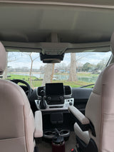 RV rental interior: dashboard, comfortable seats, and a large water bottle, with a serene lake view through the windshield.