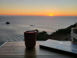Coastal RV rental sunset: A tranquil workspace with a laptop and mug on a table overlooking the ocean.