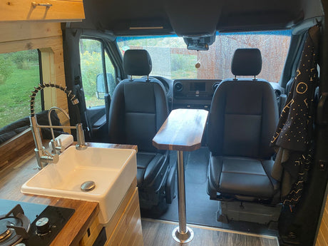 Inside an RV rental: a compact camper van interior with a kitchen (sink, stove), dining table, and front seats.