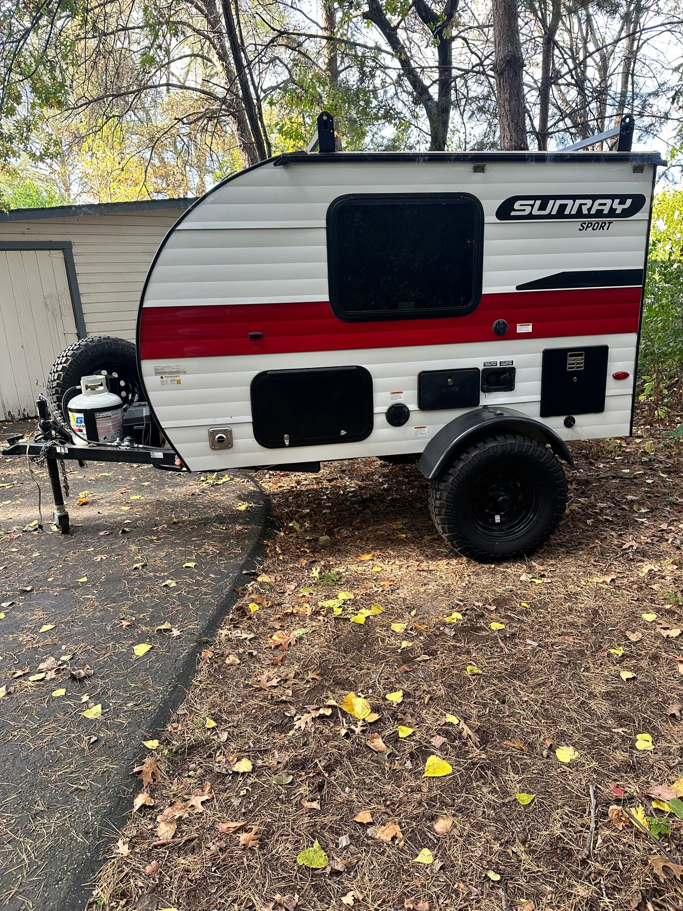 White & red Sunray Sport teardrop **rv rental**, with rugged tires, parked on a leafy drive. Perfect for adventure! — photo 13