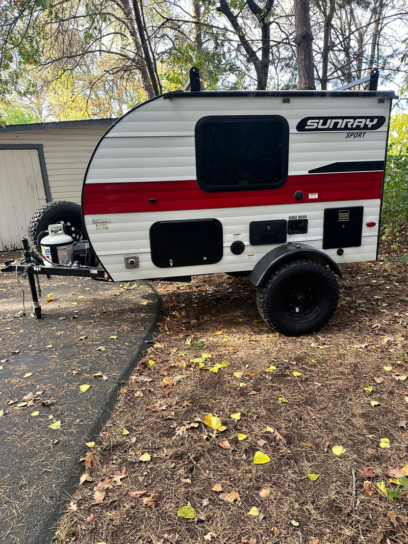 White & red Sunray Sport teardrop **rv rental**, with rugged tires, parked on a leafy drive. Perfect for adventure! — photo 13