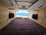 Cozy RV rental camper van interior: a bed with wood walls opens to a beautiful beach and ocean view.