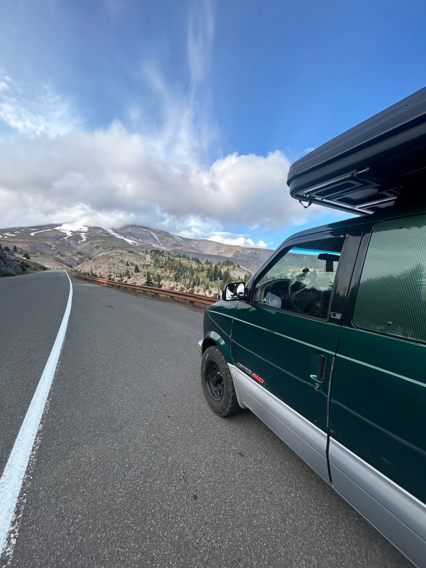 Dark green van with a rooftop tent parked on a scenic mountain road, ideal for an RV rental adventure through nature.