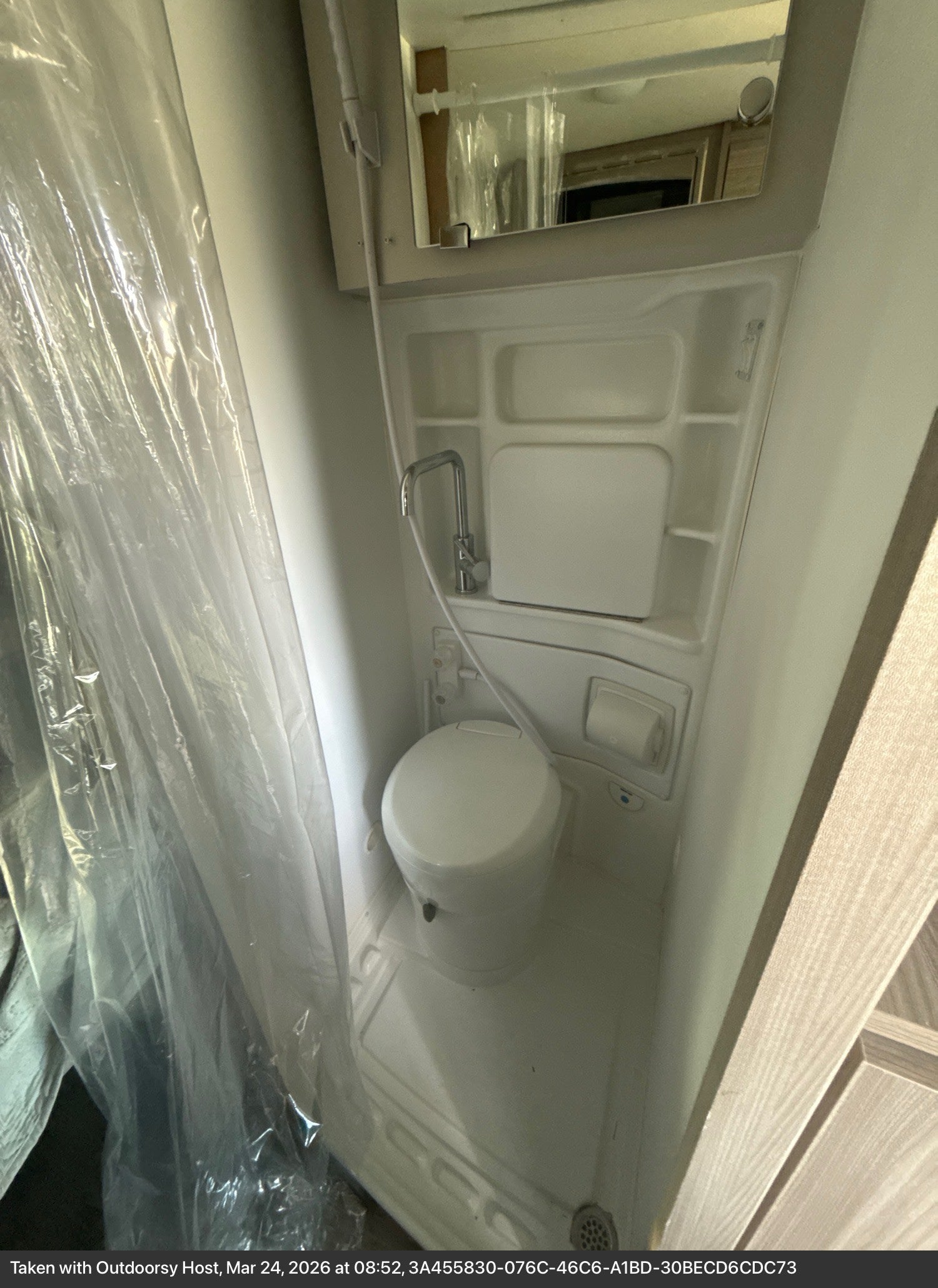 This rv rental features a compact bathroom with a toilet, shower, plastic curtain, and mirror, perfect for small spaces.