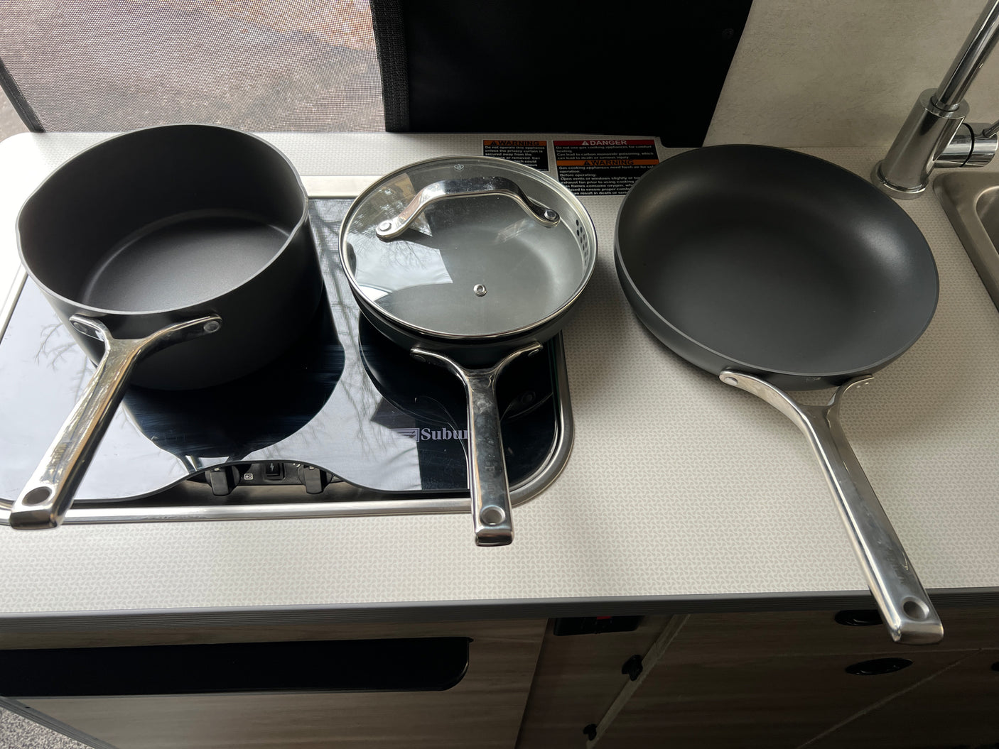 RV rental kitchen setup: Two non-stick pans, a pot, and an induction cooktop on a counter with a sink.