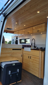 RV rental interior featuring a bright wood-paneled ceiling, comfortable bed, compact kitchenette, and a Dometic CFX cooler.