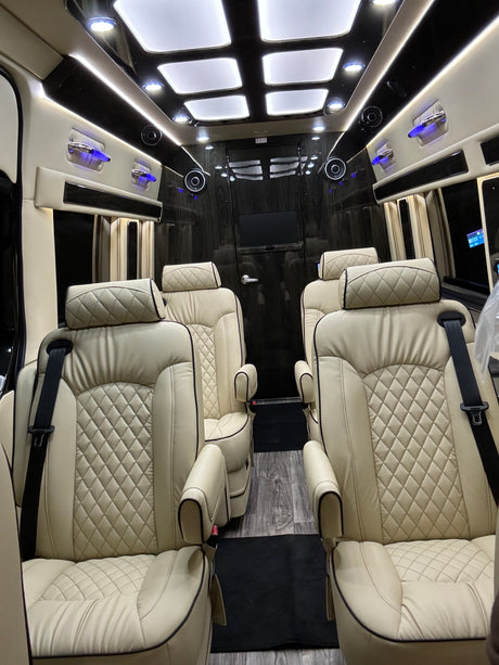 Spacious luxury RV rental interior with plush cream-colored, diamond-quilted seats, ambient lighting, and wood paneling.