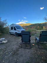 Enjoying a scenic RV rental camping trip with a camper van, chairs, and a fire pit under a clear blue sky.
