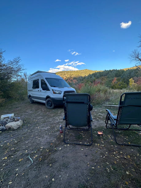 Enjoying a scenic RV rental camping trip with a camper van, chairs, and a fire pit under a clear blue sky.