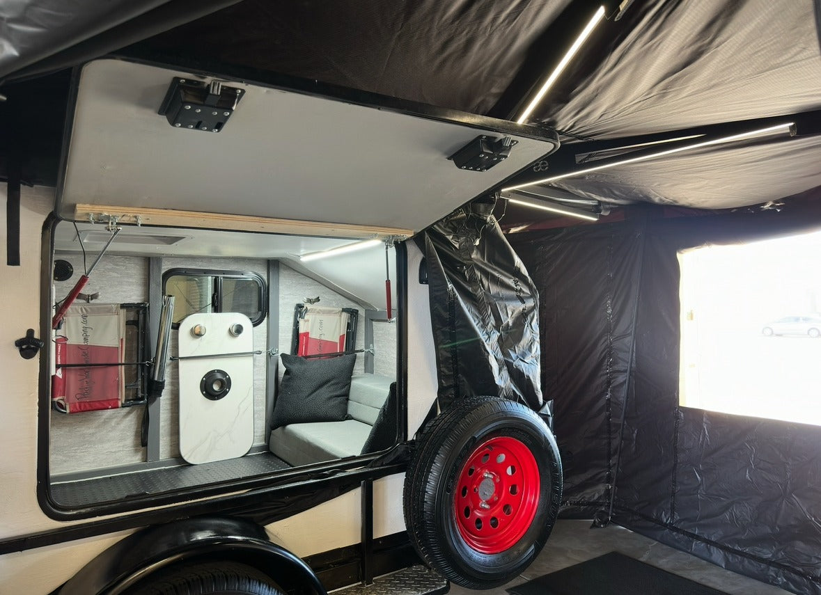 This rv rental's open side reveals a compact, cozy interior with an attached black tent and a striking red spare tire.