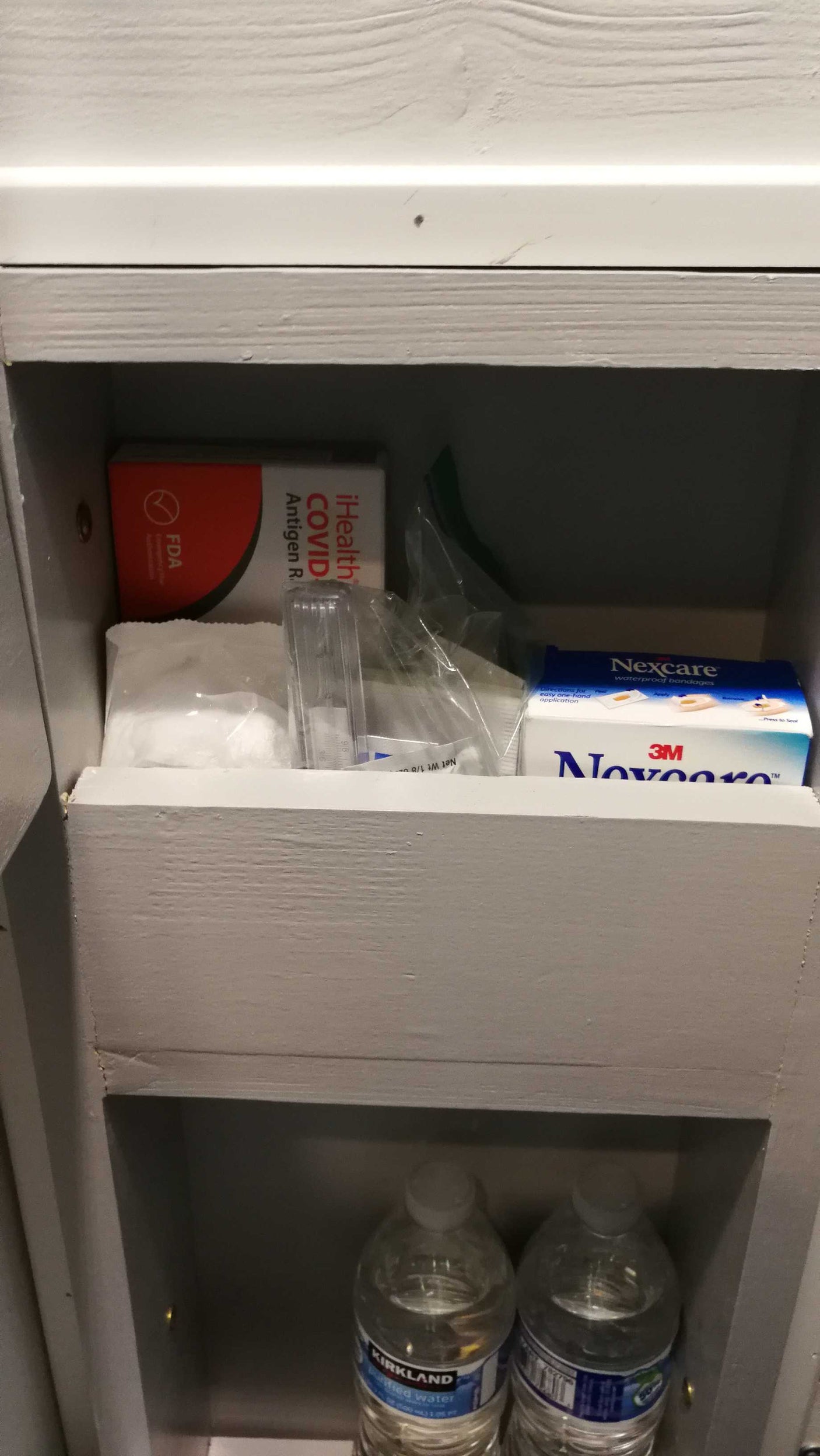 Medical supplies, including a COVID test, bandages, and water bottles, neatly stored in an RV rental cabinet.
