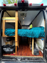 Interior view of an RV rental camper van from the back, revealing custom wooden bunk beds, a single bed, and amenities.
