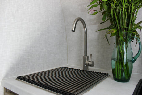 Clean RV rental kitchen area features a brushed metal faucet, a drain rack, and a glass vase with green plant stems.