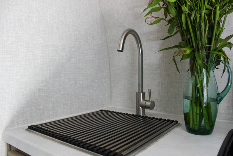 Clean RV rental kitchen area features a brushed metal faucet, a drain rack, and a glass vase with green plant stems. — photo 9