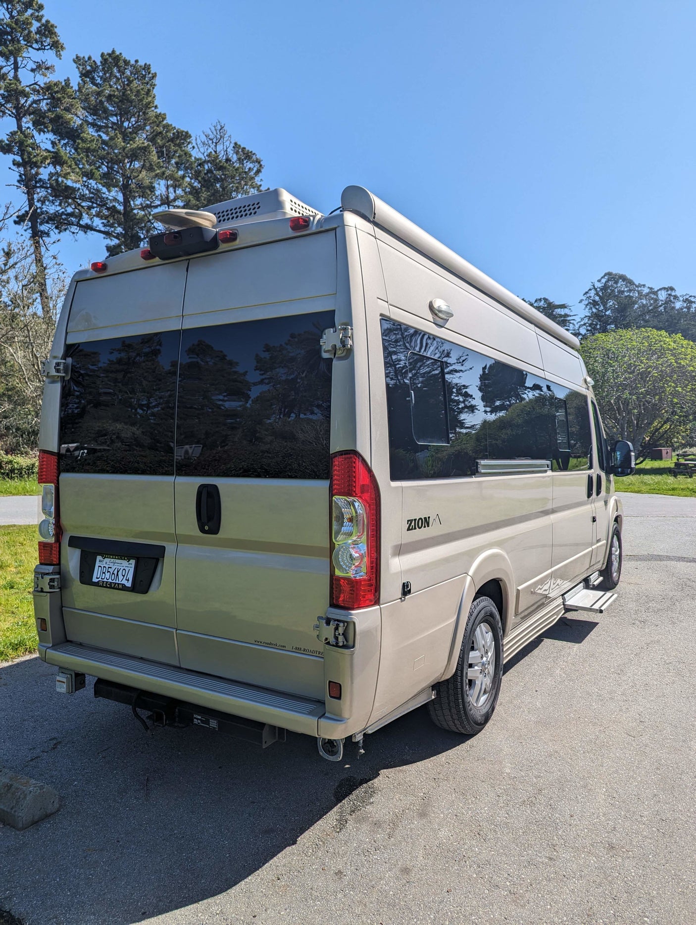 Beige Zion RV rental camper van, ready for adventure. Rear view shows side awning, roof unit, and California plate.