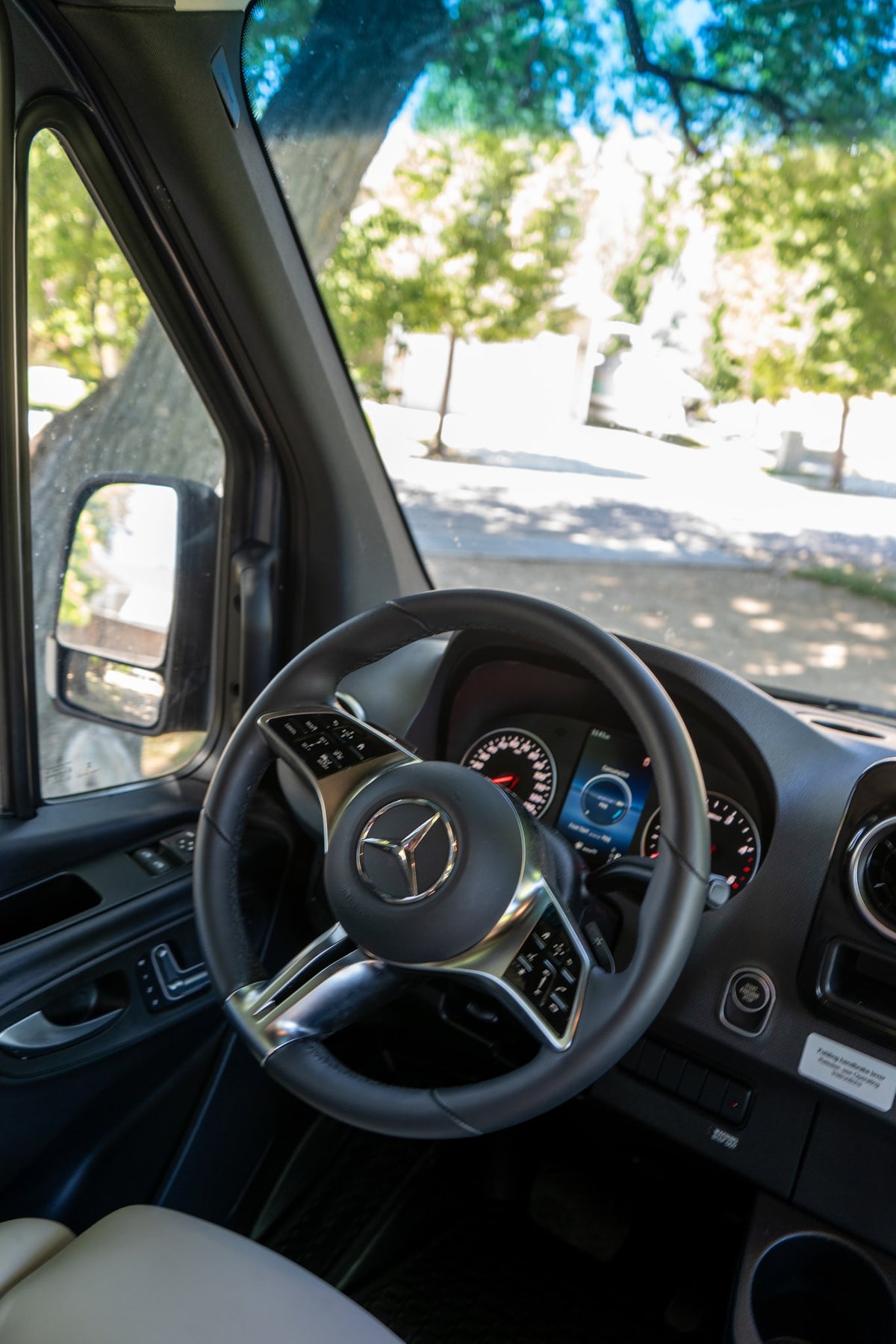 Inside an RV rental: a Mercedes-Benz steering wheel, digital dashboard, and a view of a sunny, treelined road. — photo 10