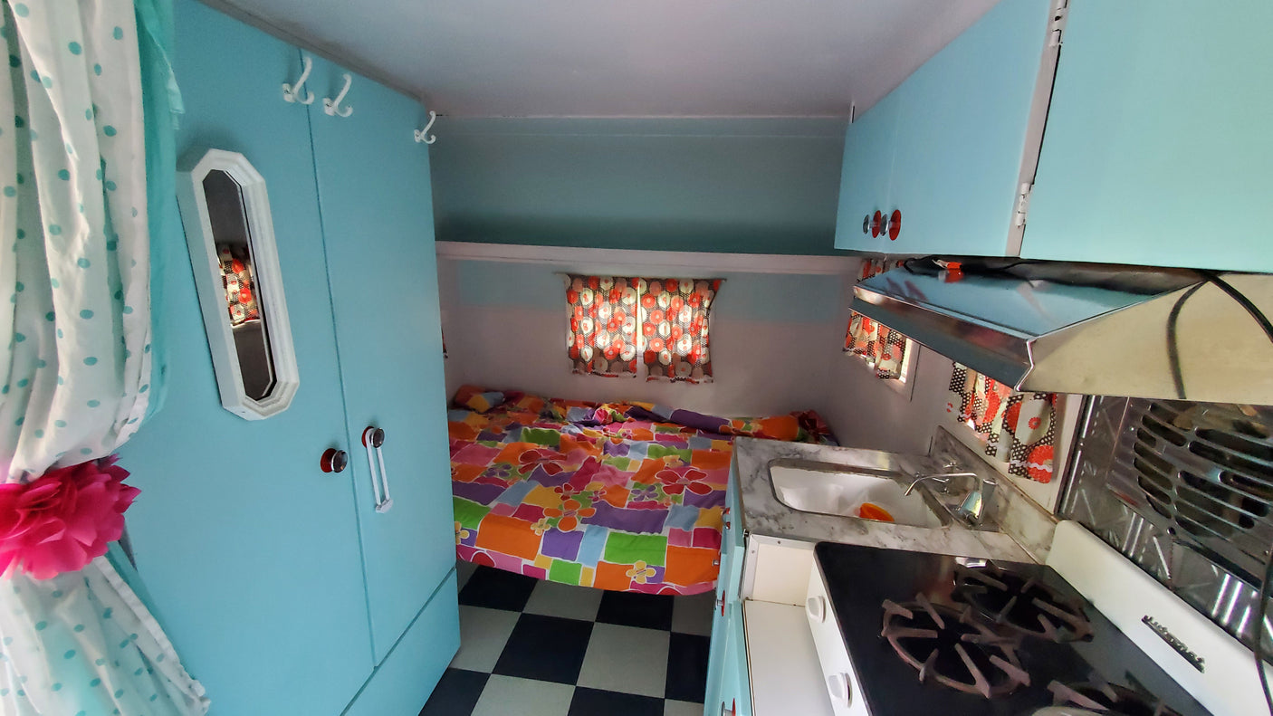 Retro rv rental interior with bright blue walls, colorful bedding, a compact kitchen, and checkered floor.