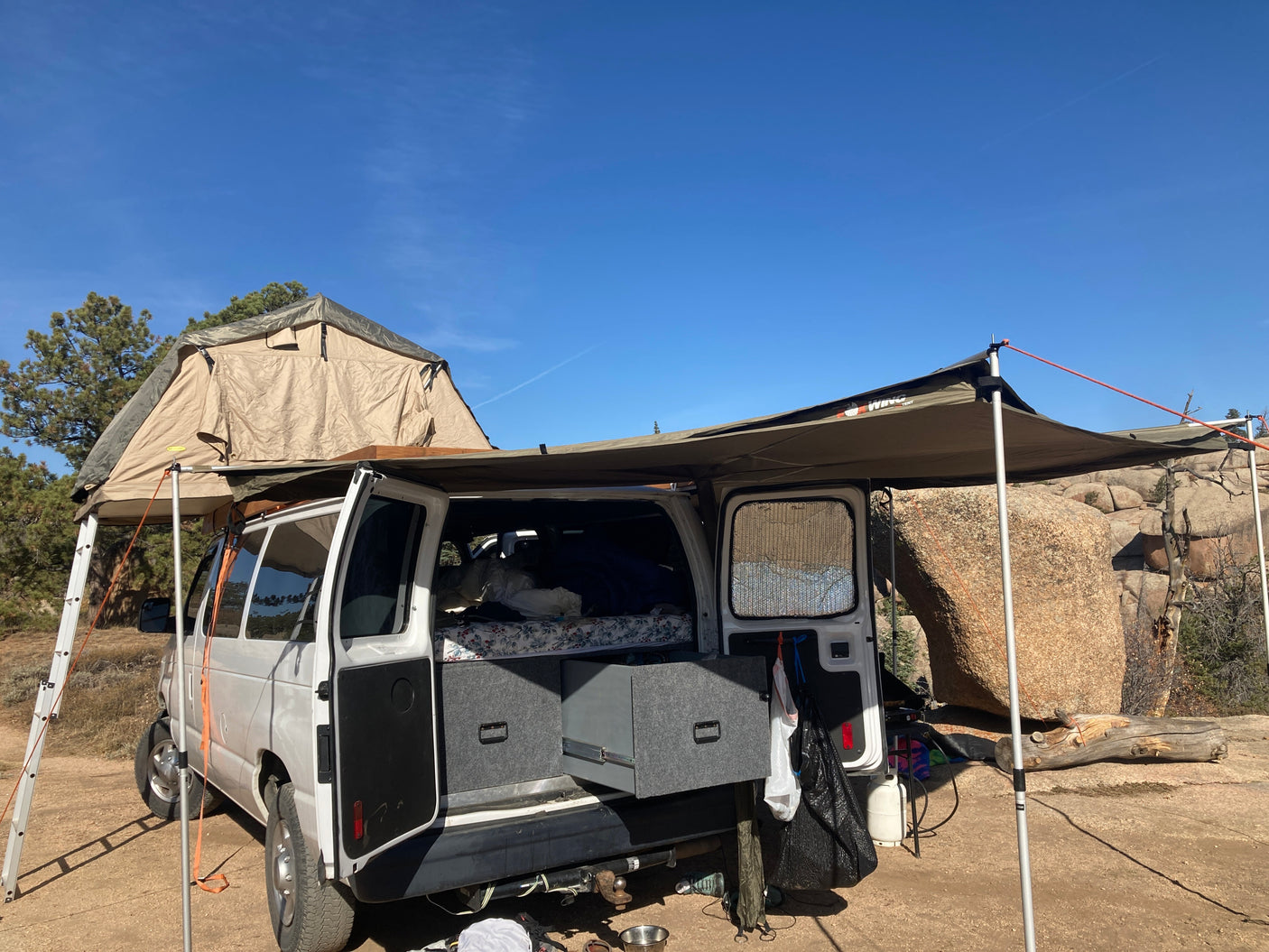 An RV rental camper van with a rooftop tent and awning deployed at a scenic rocky campsite. Perfect for outdoor adventures.