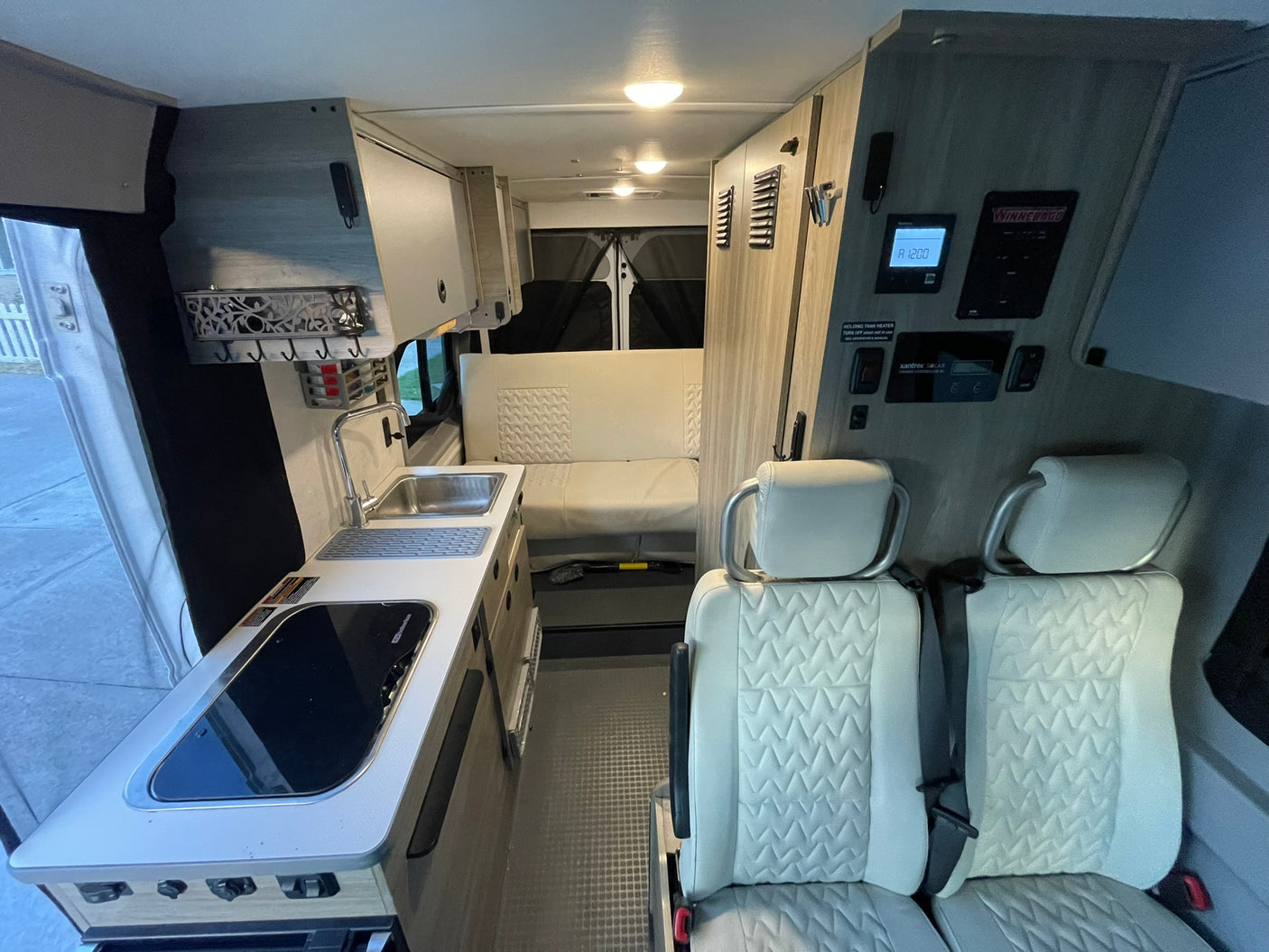 Explore this well-equipped rv rental interior: compact kitchen, modern controls, and comfortable quilted seating area.