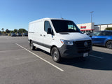 White Mercedes Sprinter van, ideal for RV rental, parked in a sunny lot. Nearby cars and an Edge Fitness building are visible.