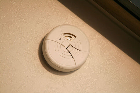 White smoke detector on a textured wall, essential for safety inside your RV rental.