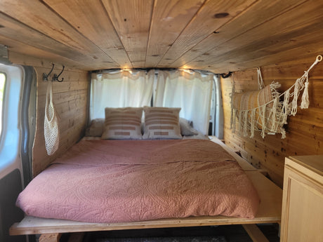 A cozy RV rental bedroom interior with light wood paneling, a pink bed, decorative pillows, and macrame accents.