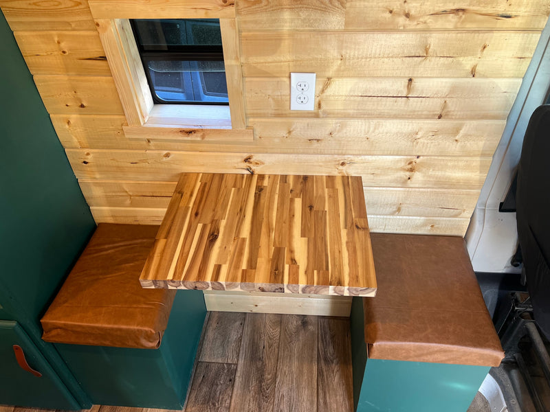 This RV rental's cozy dinette features light wood walls, a window, a butcher block table, and brown cushioned benches. — photo 10