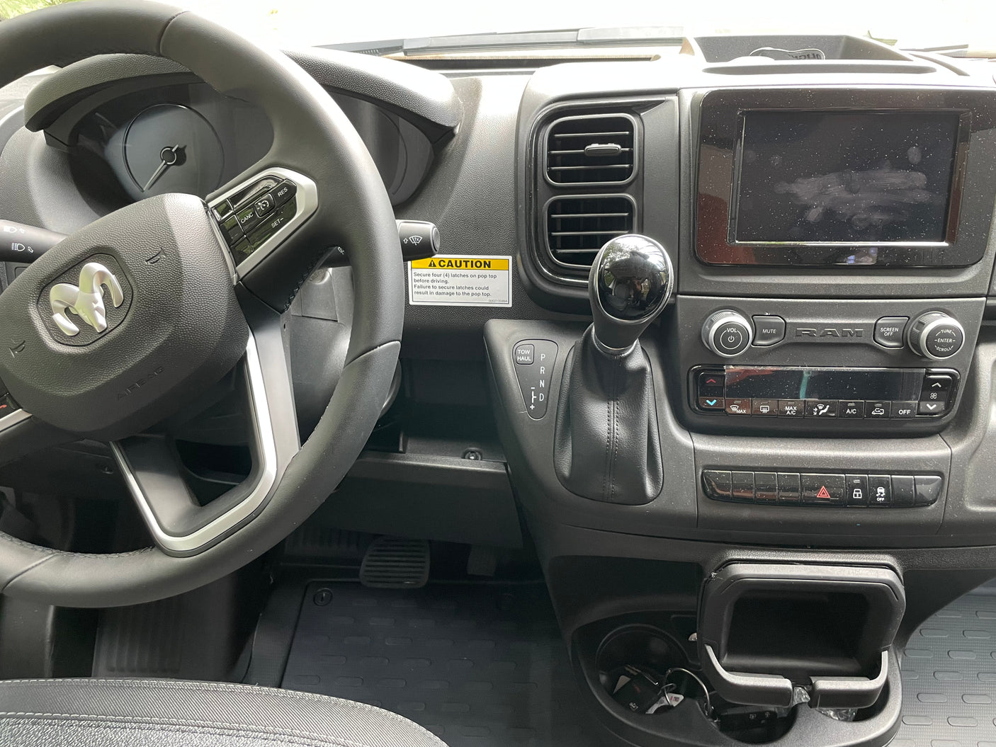 Driver's view of an RV rental dashboard, showing the steering wheel, infotainment screen, gear shifter, and controls inside the camper van.