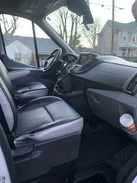 RV rental van interior: black/grey leather seats, modern dashboard, and bright window views of a neighborhood.