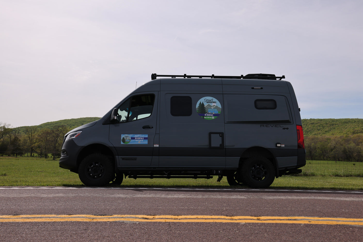 Gray Winnebago Revel 4x4 RV rental van on a road. Ready for smart adventures amidst green hills.