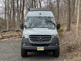 Grey Mercedes Sprinter rv rental van with off-road tires, parked on a gravel path in a forest.