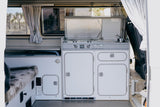 Explore this RV rental's camper van interior. Features a compact kitchen (stove, sink), bench, and desert views.