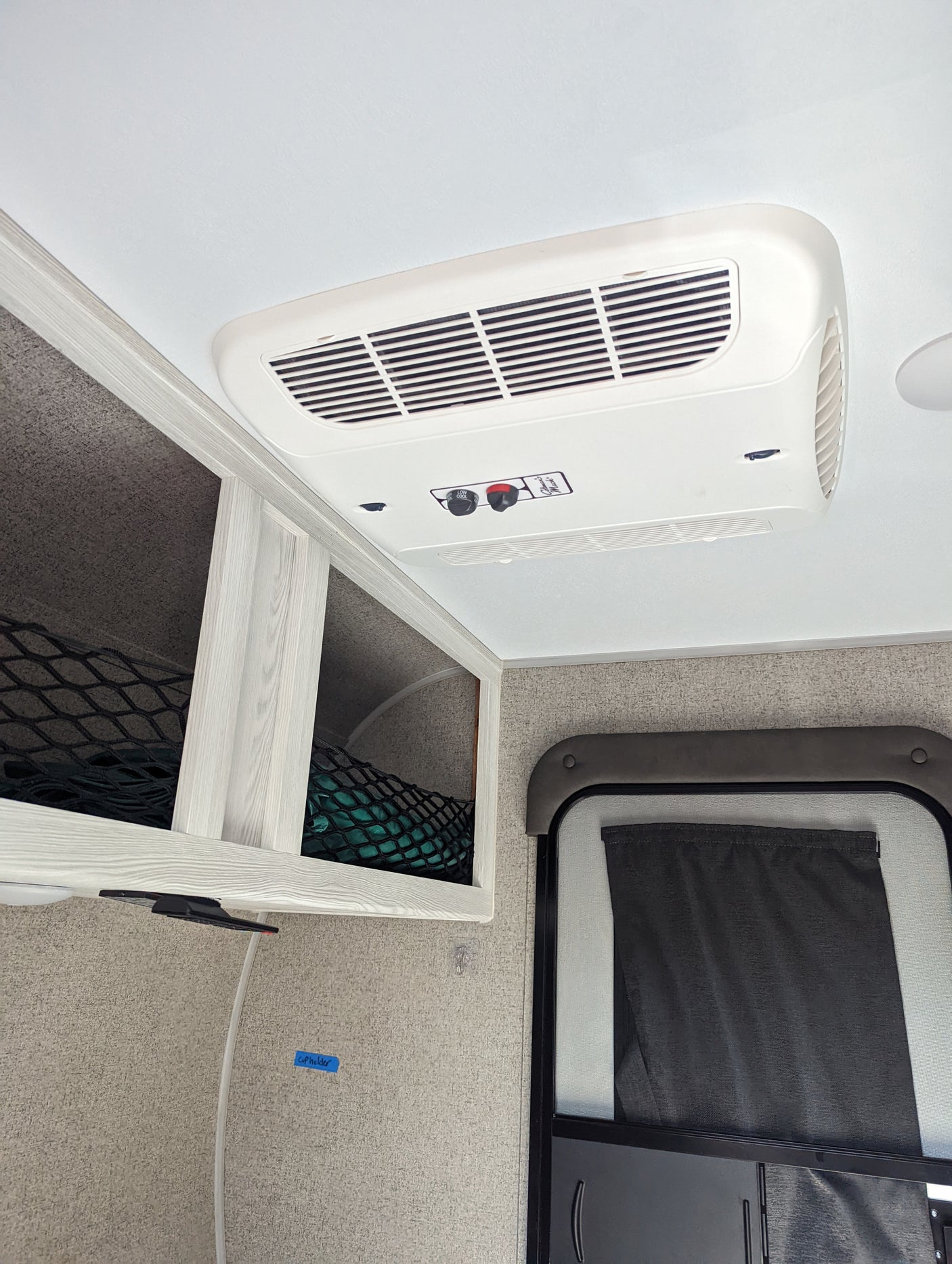 RV rental interior featuring a ceiling-mounted AC unit, overhead storage with nets, and a door with a pulled-down curtain.