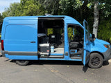 This bright blue camper van, an RV rental, has its doors open, showing the versatile interior setup.
