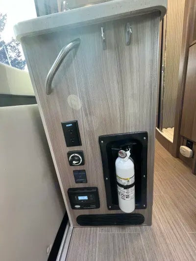RV rental interior: A light wood-look panel displays electrical outlets, system controls, and a mounted fire extinguisher. — photo 18