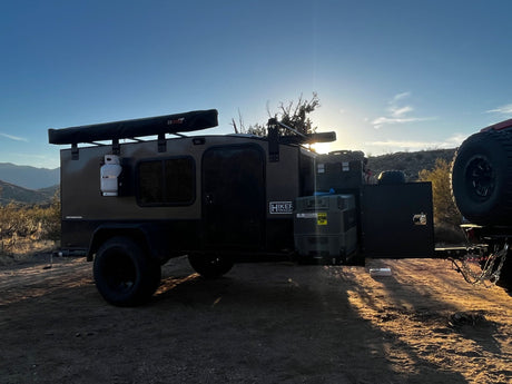 Rugged off-road teardrop camper, ideal for an RV rental, ready for sunset adventure. Gear visible in the rear hatch.