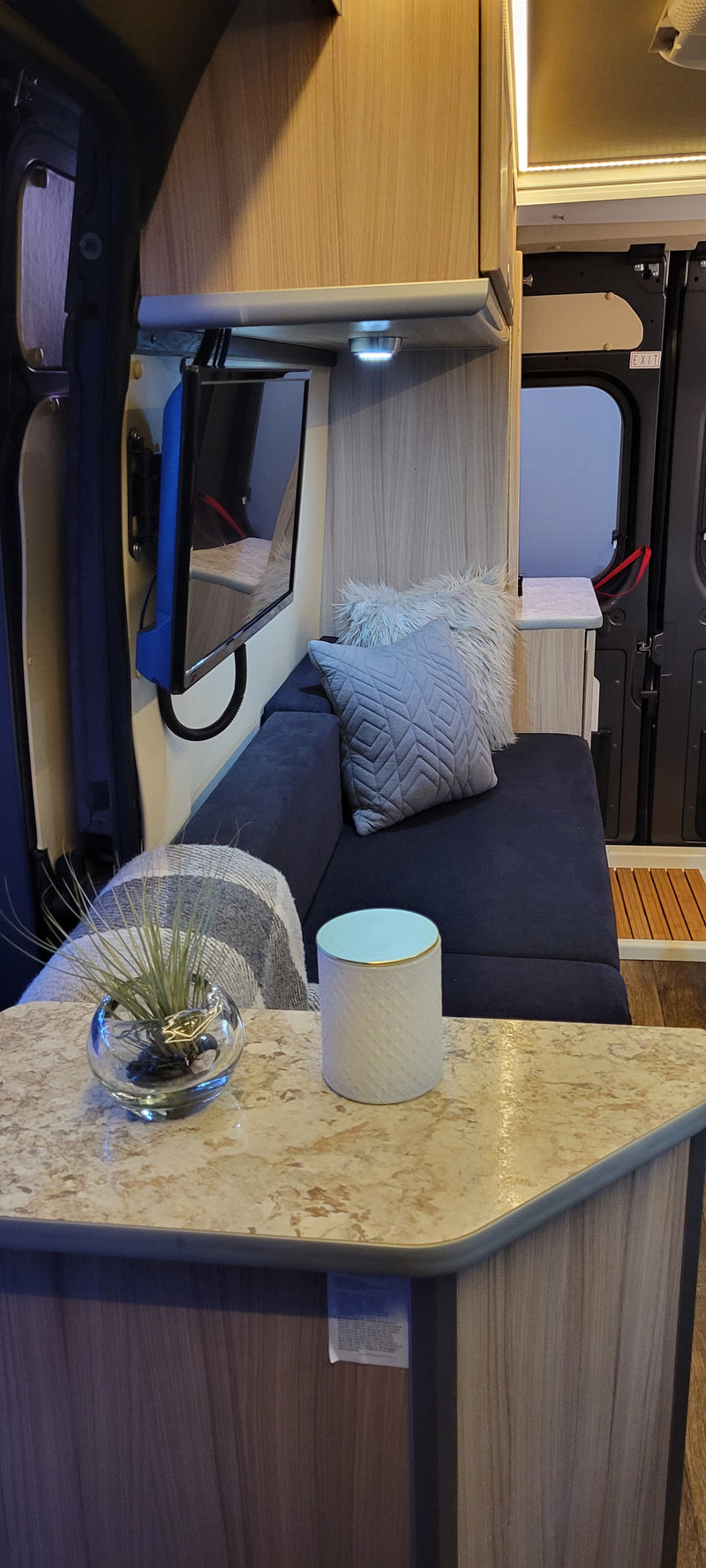 RV rental living space: a comfortable sofa, wall-mounted TV, and compact counter with decor beside the exit. — photo 17