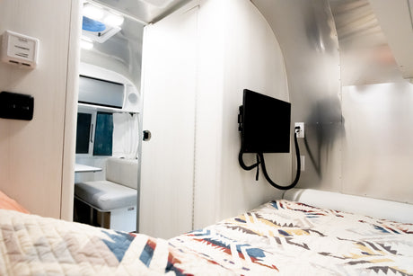 Cozy RV rental interior with a patterned bed, wall-mounted TV, and dinette area visible for comfortable living.