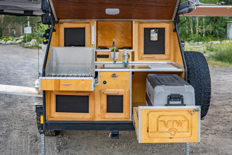 Compact outdoor kitchen of an RV rental camper, featuring a sink, stove, fridge, and storage. Perfect for mobile adventures.