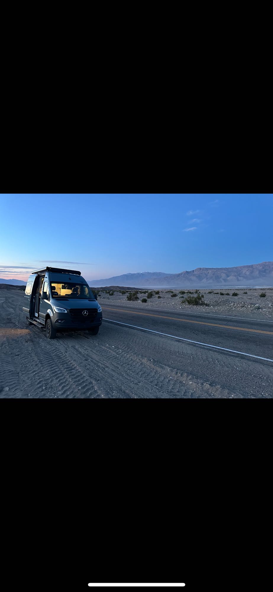  and kayak in a scenic desert.|Woman smiles from her grey RV rental|Adventure-ready Winnebago Revel 4x4 RV rental parked in scenic red rock mountains under a clear sky.|A modern grey RV rental with off-road tires — photo 7
