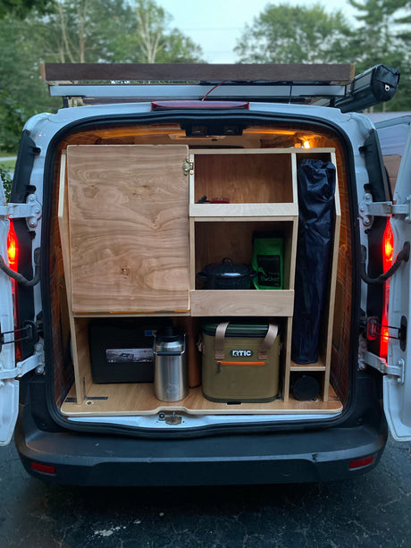 Open rear of a white van, revealing a clever wooden camper conversion. Organized storage for camping gear makes this ideal for an RV rental.