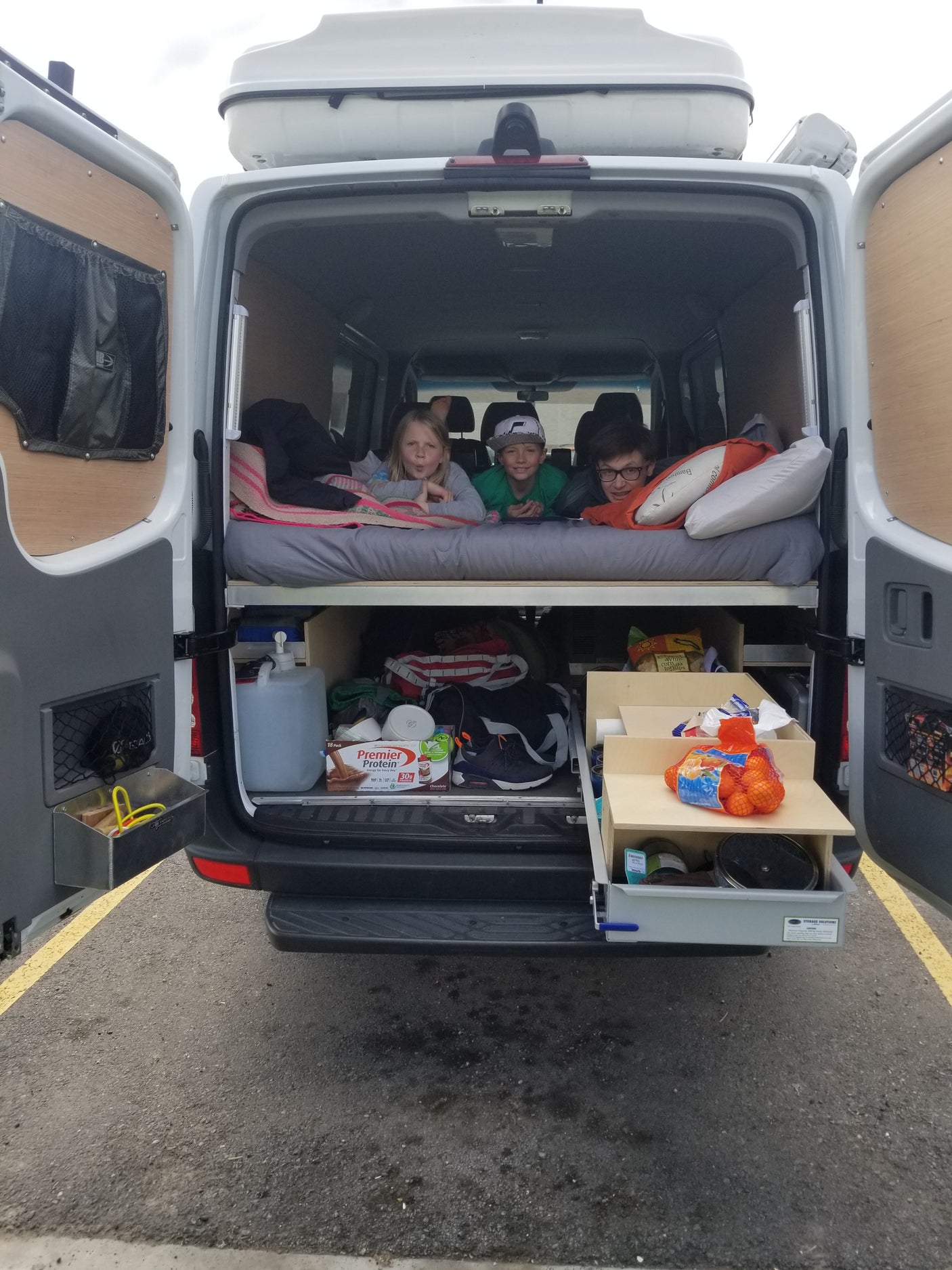 Three kids lounging in an RV rental camper van's back, showcasing its organized bed and practical under-bed storage.