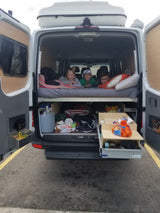 Three kids lounging in an RV rental camper van's back, showcasing its organized bed and practical under-bed storage.