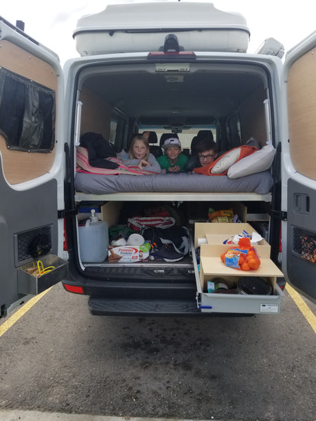 Three kids lounging in an RV rental camper van's back, showcasing its organized bed and practical under-bed storage.