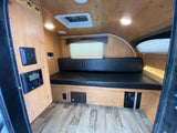 Explore this rv rental interior: light wood, black bench seat, window, control panel, and ceiling vent.